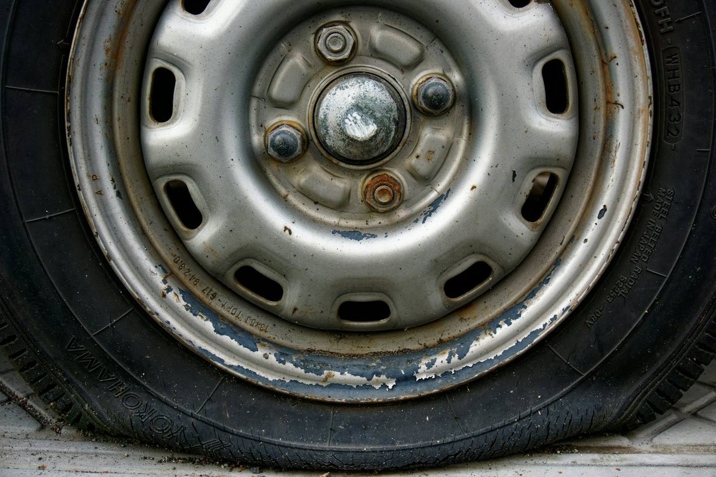Painted steel wheel with flaking finish and corrosion along the outer lip, not an alloy and not a diamond-cut face